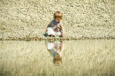 Little girl sitting on a stones-beach clipart