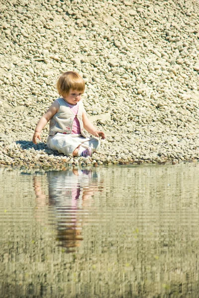 Meisje, zittend op een stenen-strand — Stockfoto