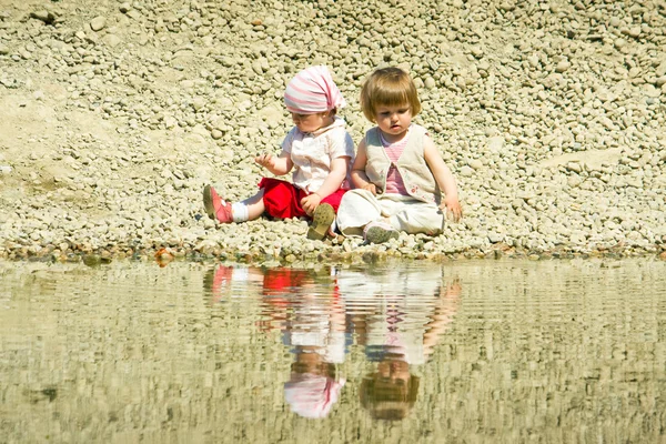 Små flickor sitter på en sten-strand — Stockfoto