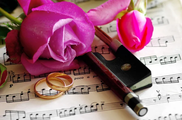 Золотые обручальные кольца и розовая роза на ноте — стоковое фото