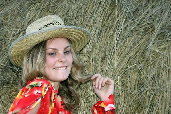 Blonde in een stro hoed tegen de hooiberg — Stockfoto