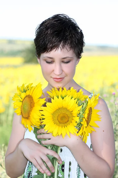 En ung flicka med en bukett solrosor på en bakgrund av gult fält — Stockfoto