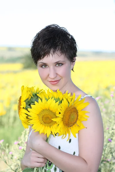 Una giovane ragazza con un mazzo di girasoli su uno sfondo di campo giallo — Foto Stock