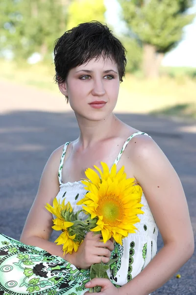 Een jong meisje met een boeket van zonnebloemen op een achtergrond van de weg — Stockfoto