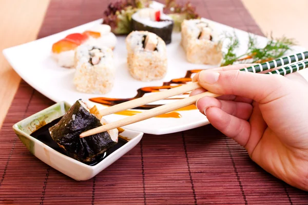 Segurando o rolo de sushi com pauzinhos — Fotografia de Stock