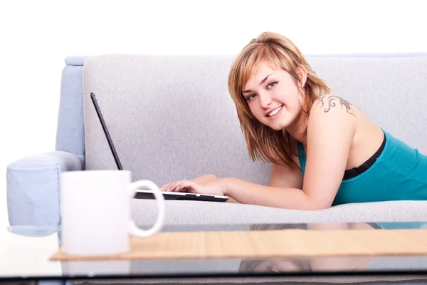 Улыбающаяся девушка на диване с ноутбуком — стоковое фото
