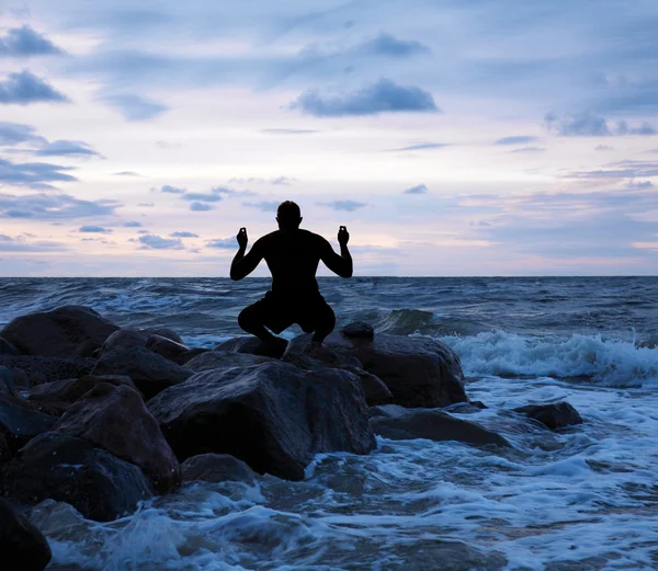 Человек медитирует на каменистом берегу моря — стоковое фото
