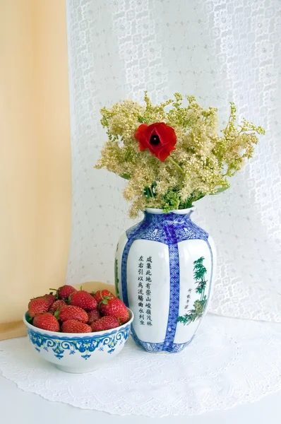 Strawberries and a vase with flowers — Stock Photo, Image