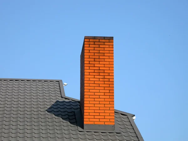 Tubulação de tijolo laranja, telhado preto, céu azul — Fotografia de Stock