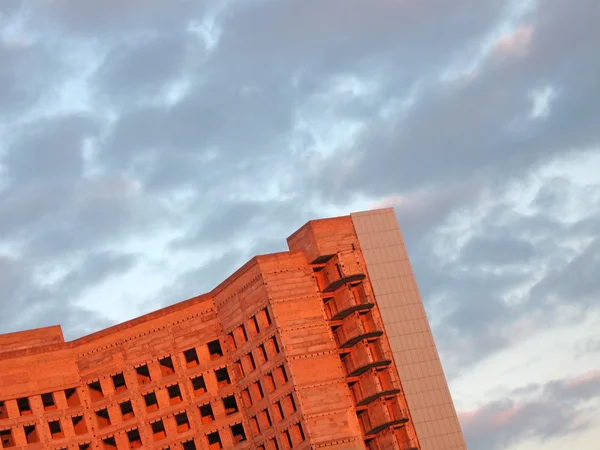Röd moderna byggnad, soluppgång, mörka moln på blå himmel. — Stockfoto