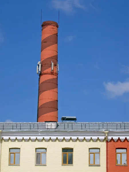Industrial brown pipe over yellow building, blue sky. — Stock Photo, Image