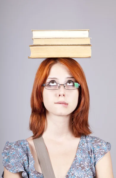 赤い髪の少女は彼女の頭の上の本を保ちます。スタジオ撮影. — ストック写真