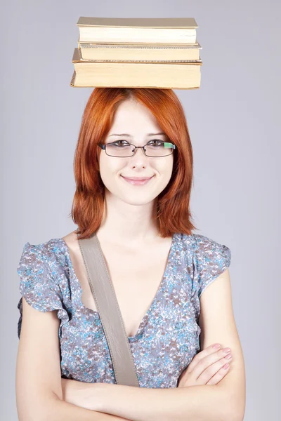 赤い髪の少女は彼女の頭の上の本を保ちます。スタジオ撮影. — ストック写真