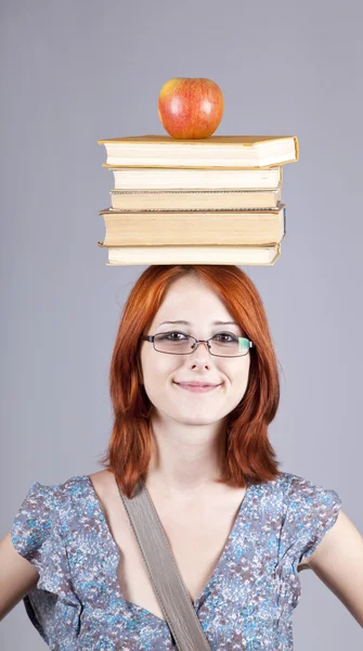 Menina ruiva manter maçã e livros em sua cabeça . — Fotografia de Stock