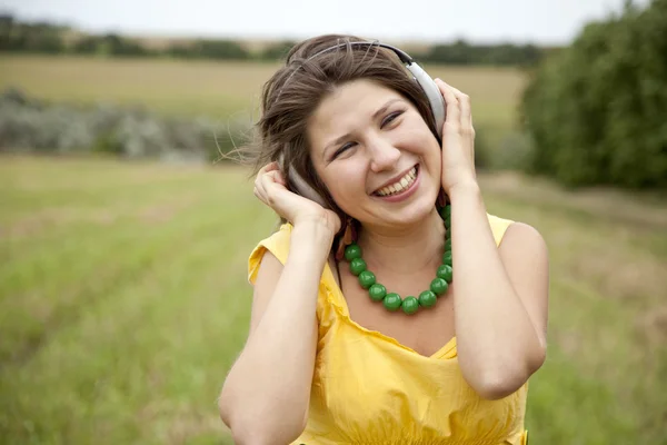 Jonge lachende mode meisje met koptelefoon op veld. — Stockfoto