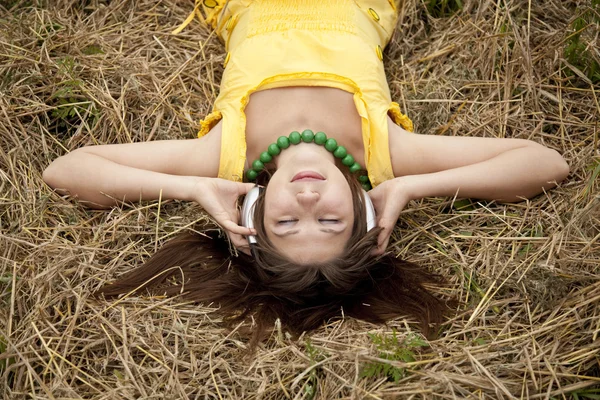 Menina bonita nova em amarelo com fones de ouvido no campo . — Fotografia de Stock