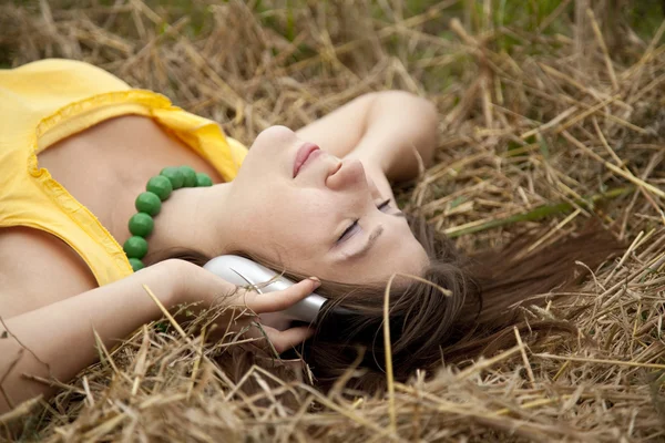 Mooi meisje in geel met koptelefoon op veld. — Stockfoto