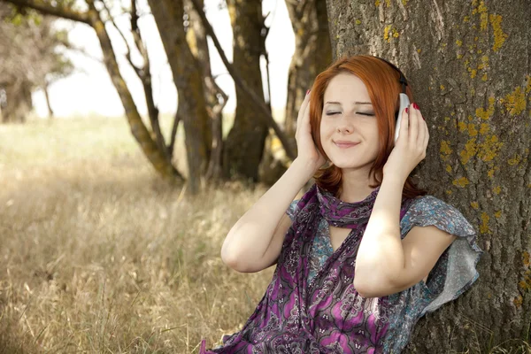 Unga leende mode med hörlurar nära träd. — Stockfoto