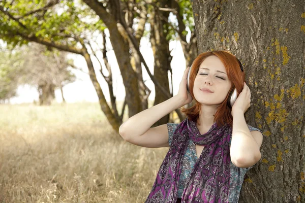 Young smiling fashion with headphones near tree. — Stock Photo, Image