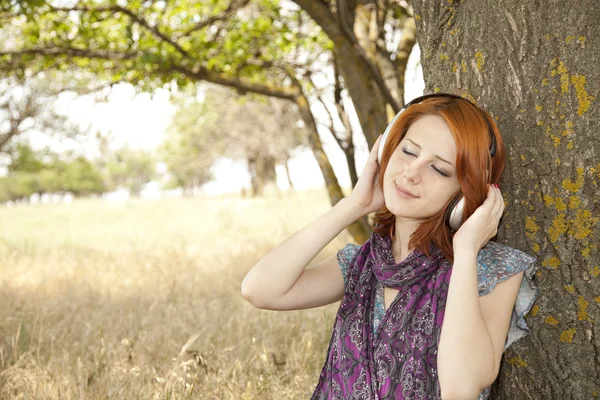 Moda joven sonriente con auriculares cerca del árbol . — Foto de Stock