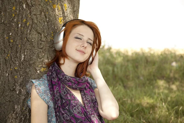 Moda sorridente jovem com fones de ouvido perto da árvore . — Fotografia de Stock