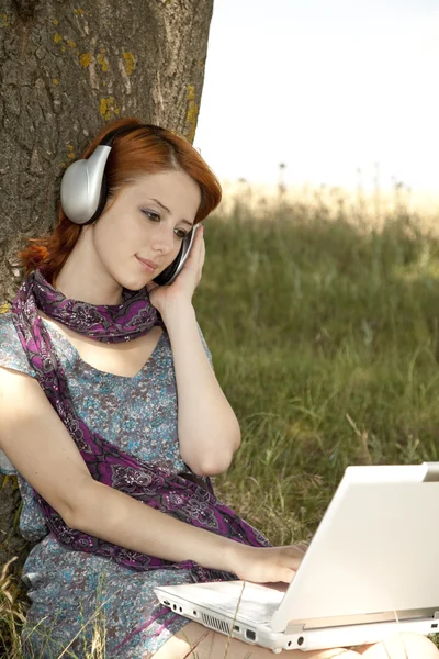 Молодая улыбающаяся модная девушка с ноутбуком и наушниками сидит — стоковое фото