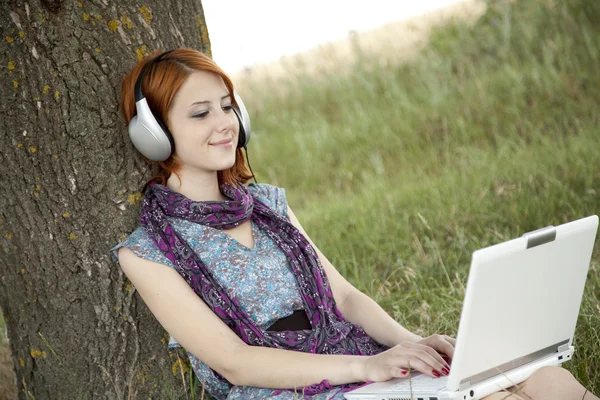 Jeune fille de mode souriante avec ordinateur portable et écouteurs assis — Photo