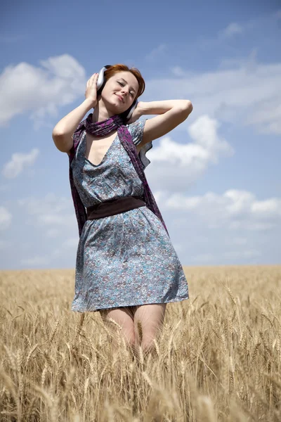 Joven chica de la moda sonriente con auriculares en el campo de trigo . — Foto de Stock