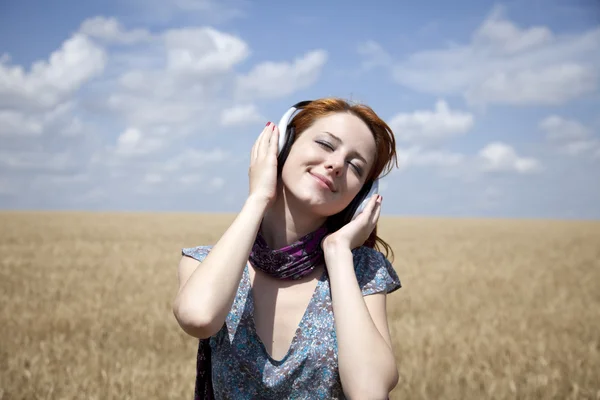 Mode-leende flicka med hörlurar på vete fält. — Stockfoto