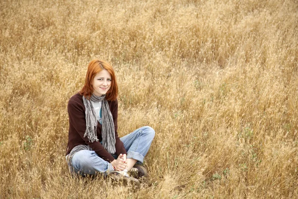 Mooi roodharig meisje zitten op gele herfst gras. — Stockfoto