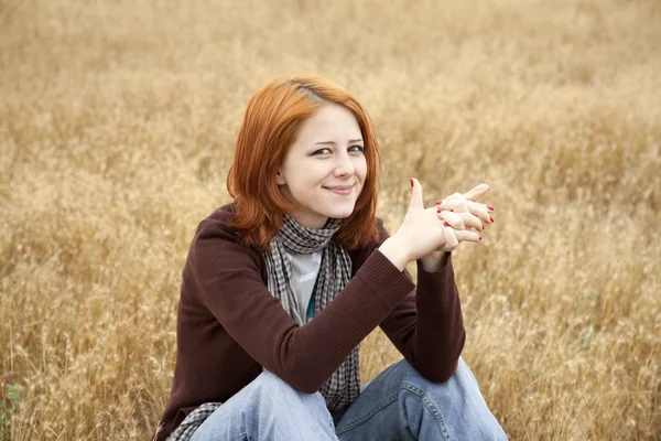 Krásná rusovlasá dívka sedí u žluté podzimní trávy. — Stock fotografie