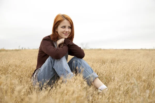 Piękna Ruda dziewczyna siedzi w żółty jesienią trawa. — Zdjęcie stockowe