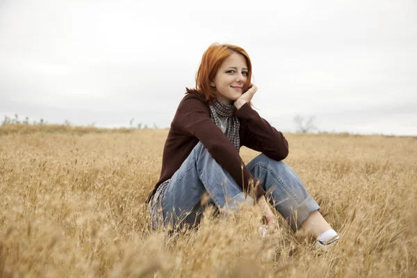 Piękna Ruda dziewczyna siedzi w żółty jesienią trawa. — Zdjęcie stockowe