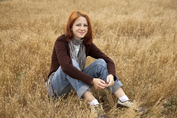 Красивая рыжая девушка сидит на желтой осенней траве . — стоковое фото