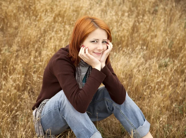 Sarı sonbahar çimlere oturup güzel kızıl saçlı kız. — Stok fotoğraf