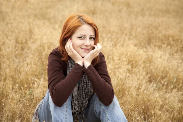 Beautiful red-haired girl sitting at yellow autumn grass. — Stock Photo, Image