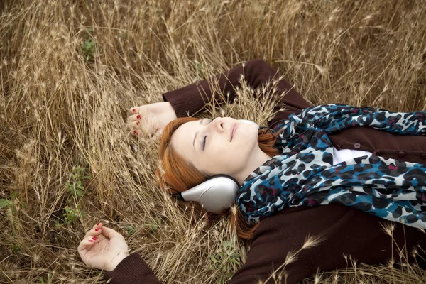 Young smiling fashion with headphones lying at field. — Stock Photo, Image