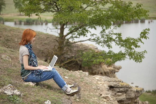 Όμορφη κοπέλα με το laptop στο βράχο κοντά στη λίμνη και το δέντρο. — Φωτογραφία Αρχείου