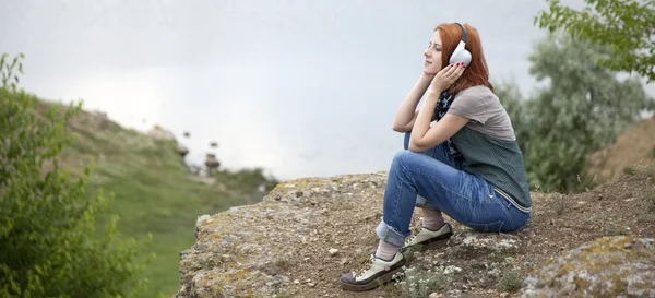 湖近くの岩で、ヘッドフォンと若者のファッションの女の子. — ストック写真