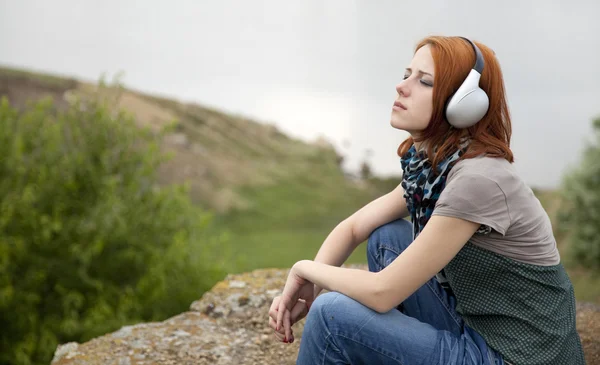Jonge mode meisje met koptelefoon op rock in de buurt van lake. — Stockfoto