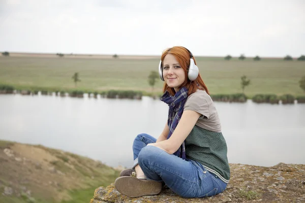 Mladá móda dívka s sluchátka na skále poblíž jezera. — Stock fotografie