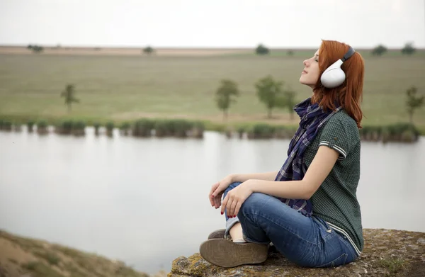 Menina de moda jovem com fones de ouvido na rocha perto do lago . — Fotografia de Stock