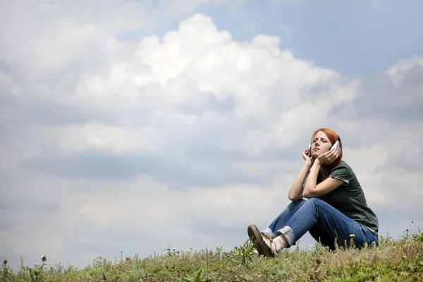 年轻的微笑女孩用耳机坐在绿色 grasss. — 图库照片