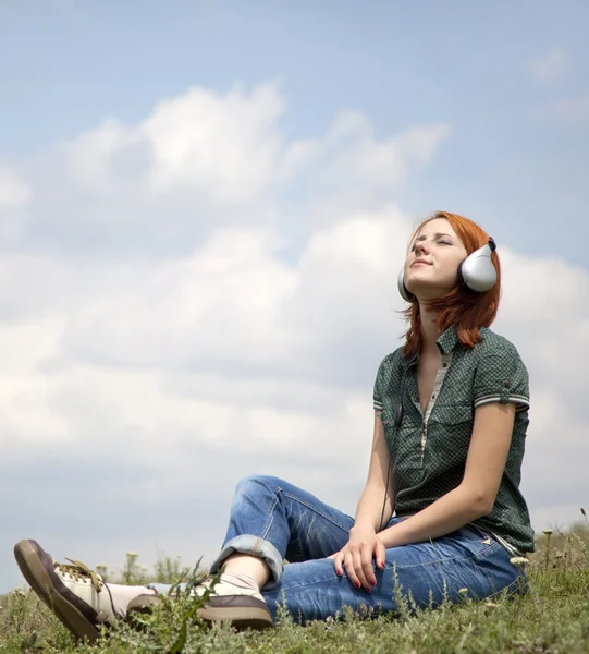 Junges lächelndes Mädchen mit Kopfhörern sitzt auf grünem Rasen. — Stockfoto