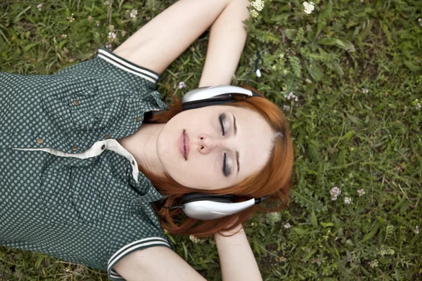 Kulaklıklarla yeşil çimlere yatan genç moda kız. — Stok fotoğraf