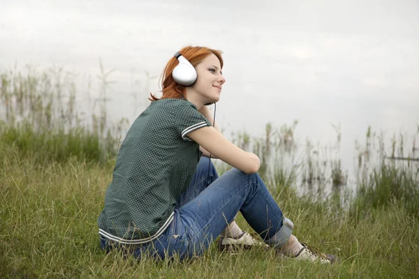Jonge mode meisje met koptelefoon zitten aan lake kust. — Stockfoto
