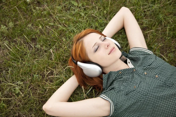 Menina de moda jovem com fones de ouvido deitado na grama verde . — Fotografia de Stock