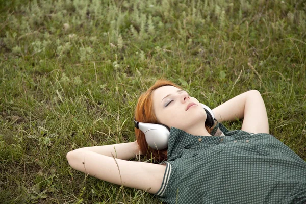 緑の芝生で横になっているヘッドフォンと若者のファッションの女の子. — ストック写真