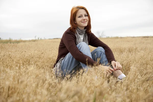 Beautiful red-haired girl sitting at yellow autumn grass. Stock Image