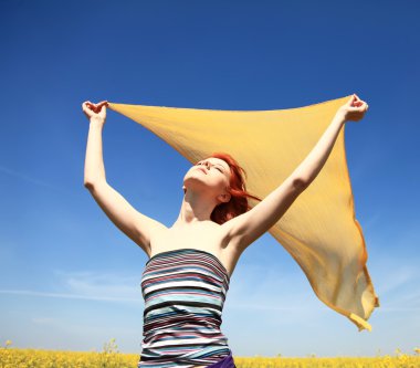 Young woman with open arms keep yellow silk on wind at rape field. clipart